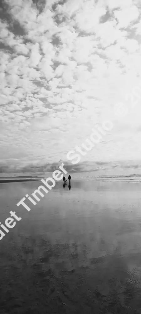 Two people walking on a beach with a large, cloud-filled sky.